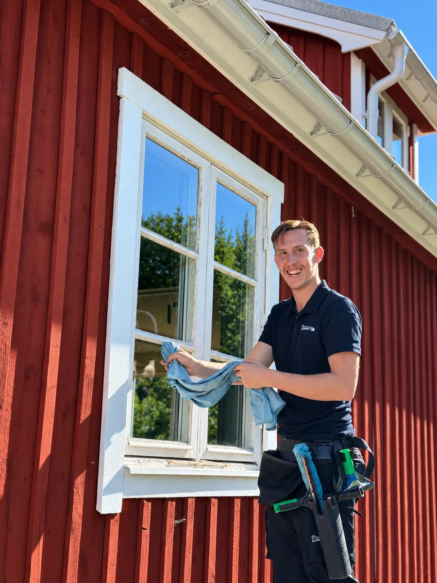 Erik putsar fönster vid en röd träfasad